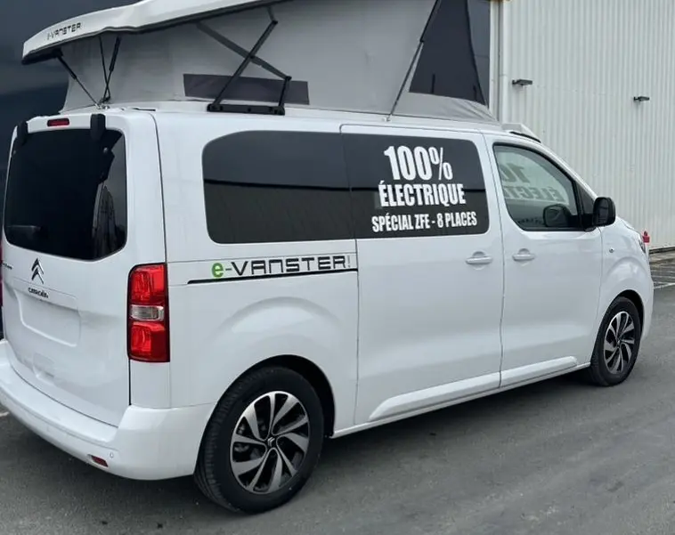 Vue 3/4 arrière droite du Citroën Jumpy blanc avec toit relevable et marquage "100% électrique" sur la vitre latérale.