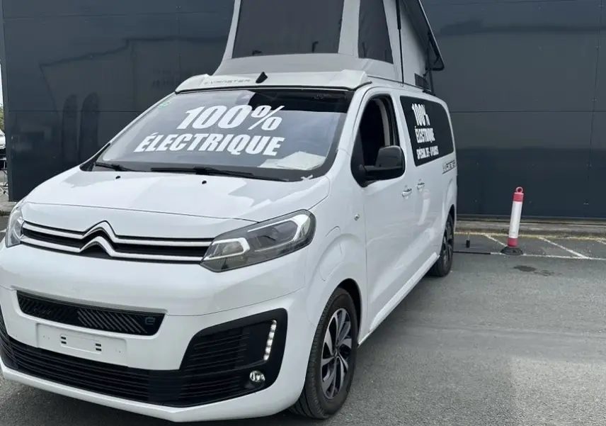 Vue 3/4 avant droit d'un Citroën Jumpy van blanc électrique avec toit relevable et marquage "100% électrique" visible.