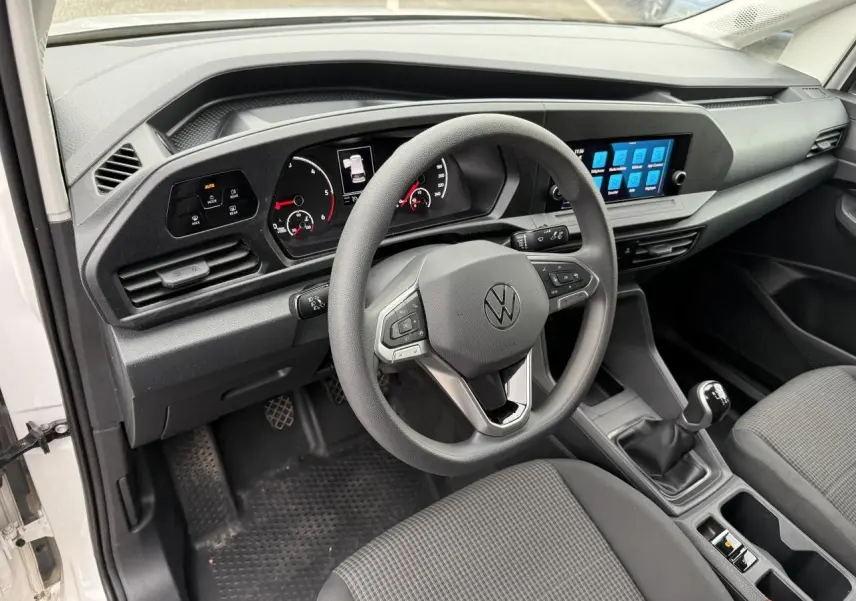 Vue intérieure du tableau de bord et volant multifonctions du Volkswagen Caddy Maxi Cargo blanc, avec écran tactile et boîte manuelle.