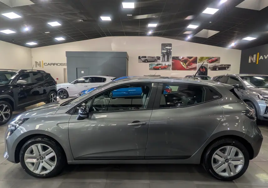 Profil côté gauche d'une Renault Clio V Blue dCi 100 CH Evolution gris schiste, en intérieur, avec jantes alliage et rétroviseurs noirs.