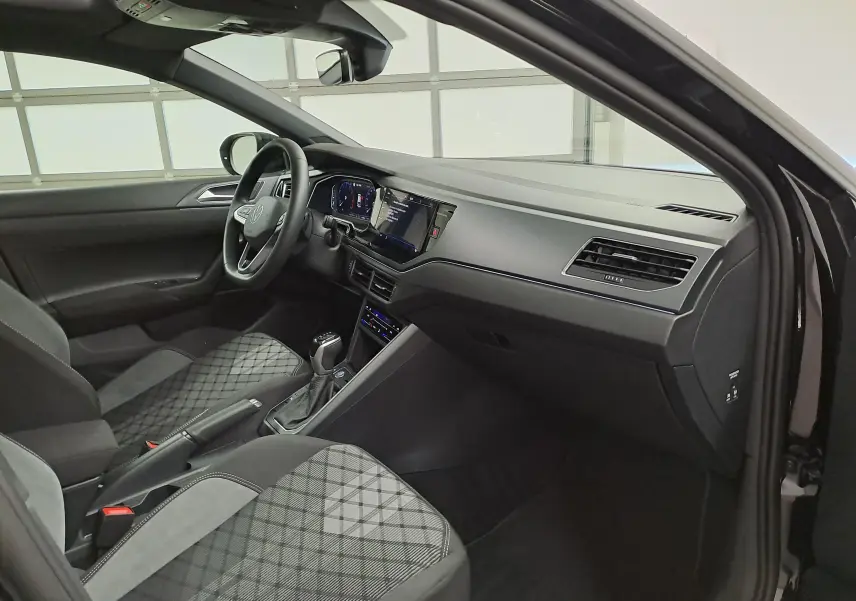 Vue intérieure côté passager avant du Volkswagen Taigo noir intense nacré, avec tableau de bord moderne et sièges tissu à motifs.