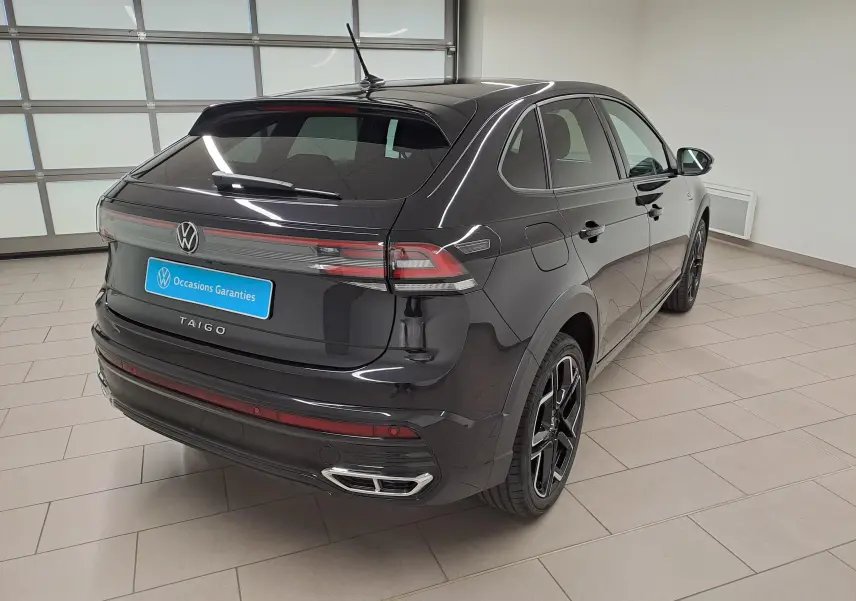 Vue 3/4 arrière droite d'un Volkswagen Taigo noir intense nacré avec jantes alliage et feux arrière LED en intérieur showroom.