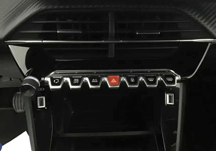 Gros plan sur la console centrale noire brillante du Peugeot 208 2022 avec boutons chromés et bouton rouge d'alerte.