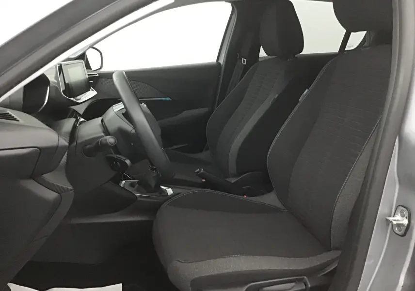 Vue intérieure côté conducteur de la Peugeot 208 2022 gris Artense, sièges tissu noir et tableau de bord moderne.