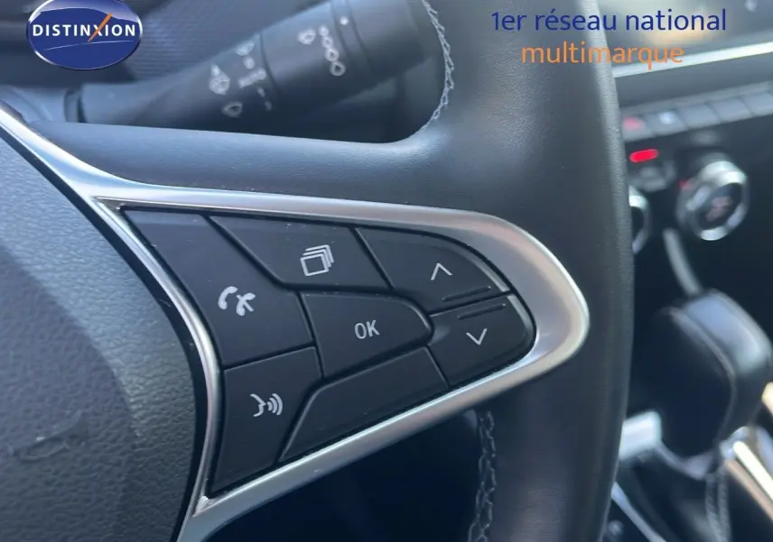 Gros plan sur les commandes au volant noir du Renault Arkana hybride 2023, avec détails chromés et console en arrière-plan.