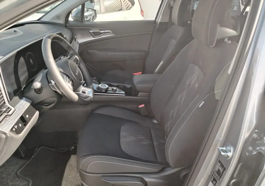 Vue intérieure côté conducteur du Kia Sportage gris perle 2025, avec sièges noirs et tableau de bord moderne.