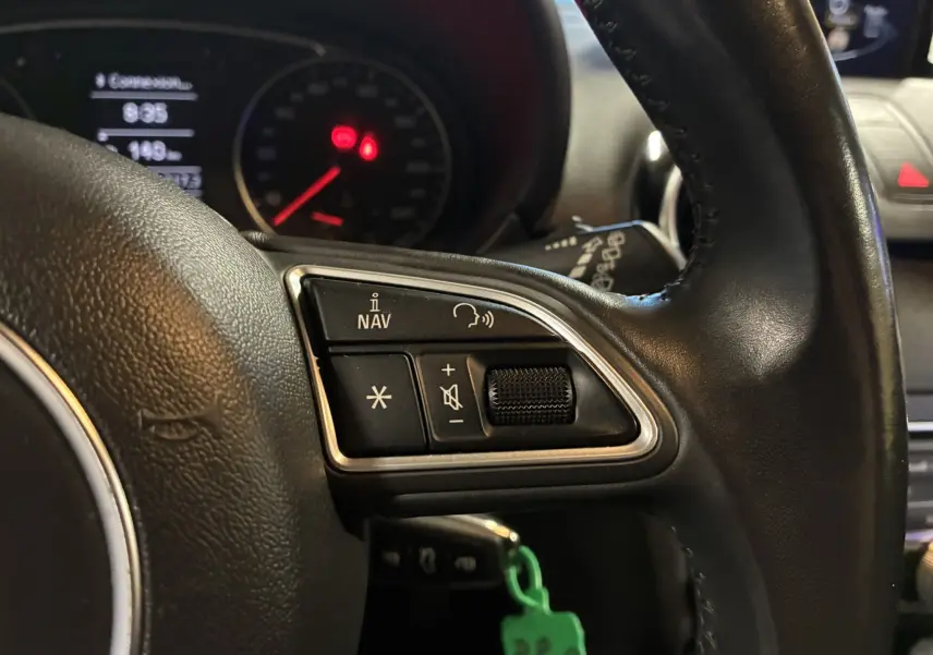 Gros plan sur les commandes gauche du volant noir d’une Audi A1 1.0 TFSI S-Line 2016, avec tableau de bord en arrière-plan.