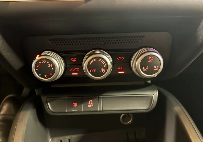 Gros plan sur les commandes de climatisation de l'Audi A1 noire, avec réglages en rouge et boutons rotatifs métalliques.