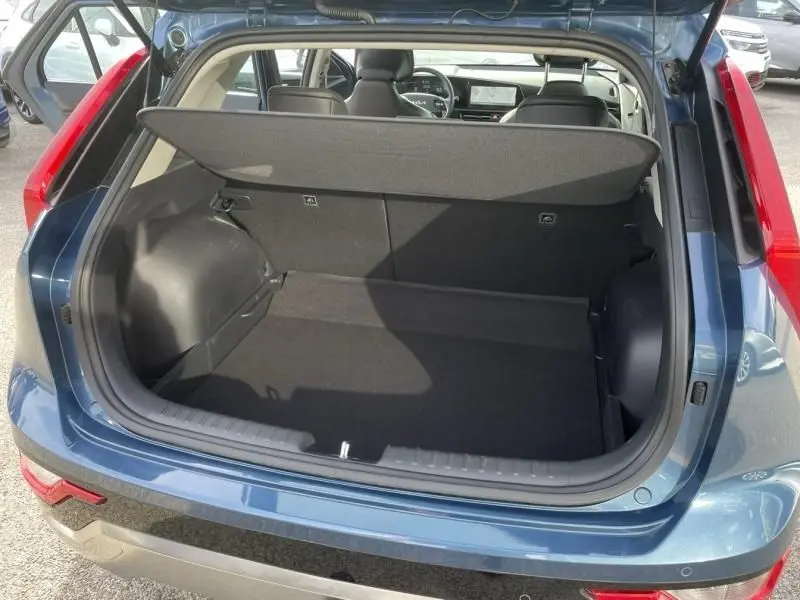 Coffre ouvert vu de l'arrière d'un KIA Niro 2024 bleu métal, montrant l'espace de chargement et l'intérieur du véhicule.