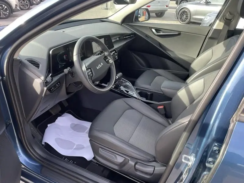 Vue intérieure côté conducteur du KIA NIRO 2024 bleu métal, montrant le volant multifonction et les sièges en tissu gris.