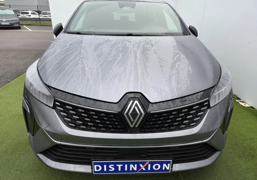 Vue frontale d'une Renault Clio gris schiste métal avec calandre noire et logo Renault proéminent, carrosserie mouillée.