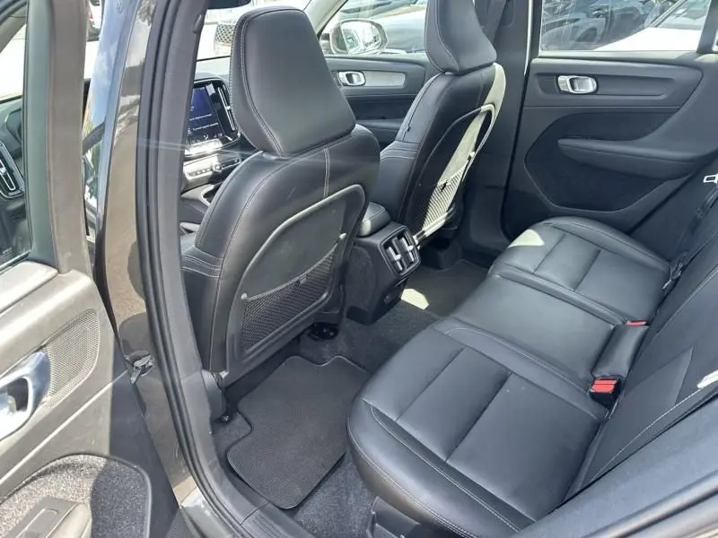Vue intérieure arrière côté gauche du Volvo XC40 gris foncé, sièges en cuir noir et aérateurs centraux visibles.