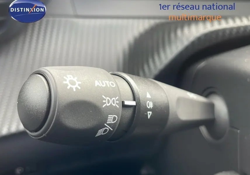 Gros plan sur la commande des phares du Peugeot 2008 2024, avec marquages blancs sur plastique noir texturé.