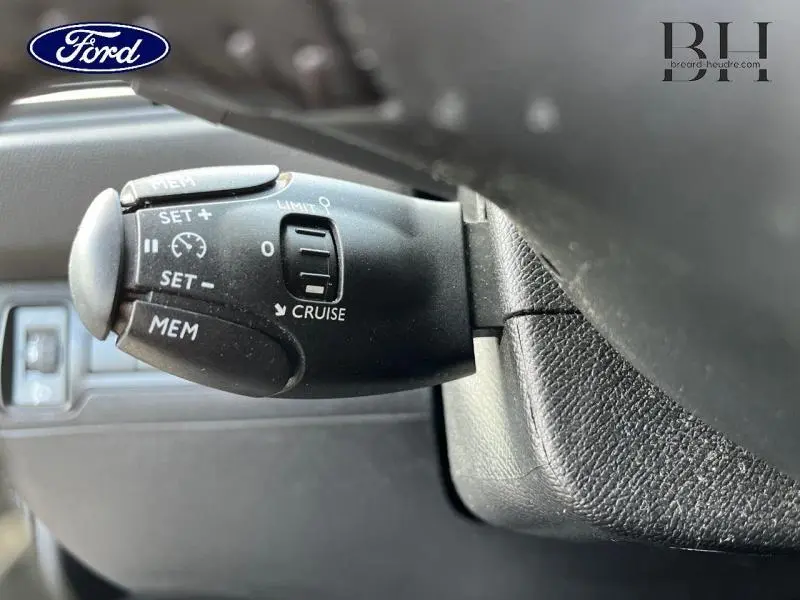 Gros plan sur la commande de régulateur de vitesse noire à gauche du volant dans l'habitacle d'une Peugeot 308 SW gris Artense.