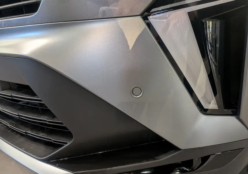 Gros plan sur le pare-chocs avant gris Cassiopé du Renault Symbioz E-TECH, mettant en valeur un capteur de stationnement circulaire.