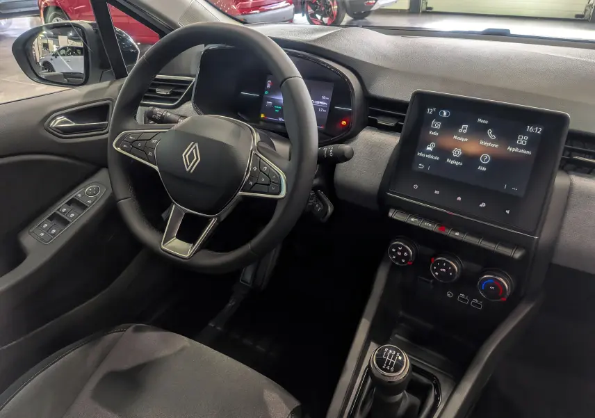 Vue intérieure côté conducteur de la Renault Clio V blanche Glacier, avec volant multifonction et écran tactile central allumé.