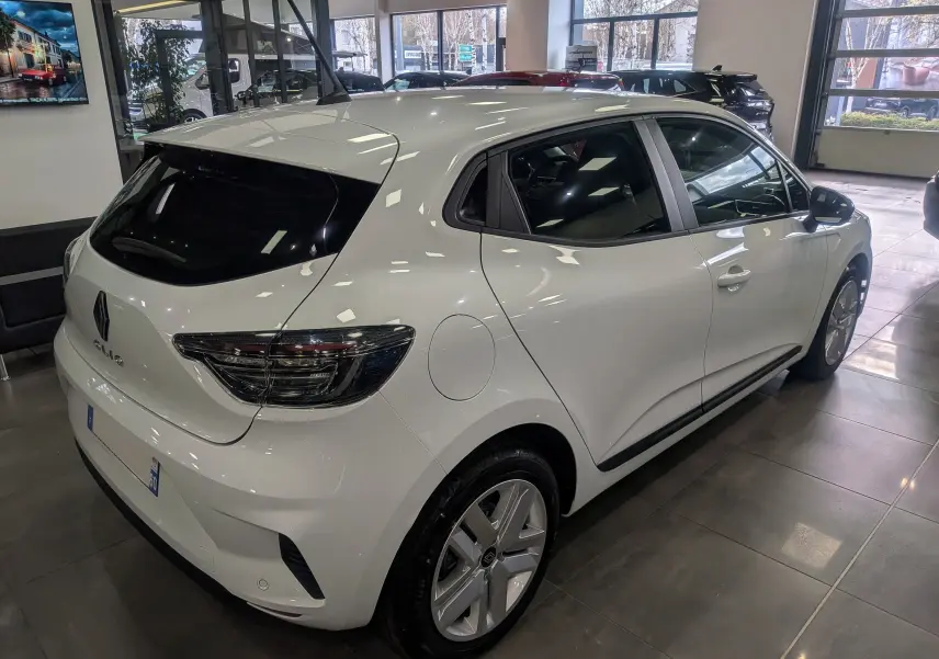 Renault Clio V Blue dCi 100 en Blanc Glacier vue 3/4 arrière droit en intérieur, feux arrière fumés et jantes alliage.