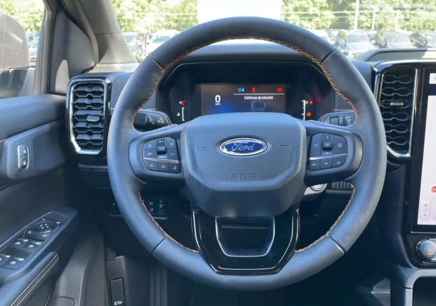 Vue intérieure centrée sur le volant cuir noir avec surpiqûres marron du Ford Ranger 2025, tableau de bord et commandes visibles.