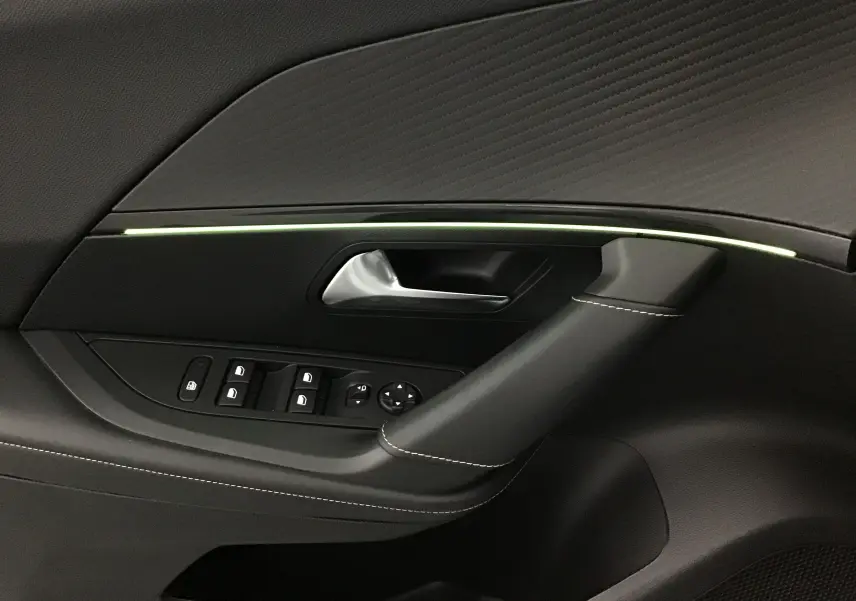 Gros plan sur la garniture intérieure côté gauche d'une Peugeot 2008 GT 2021 avec éclairage d'ambiance vert pâle et coutures blanches.