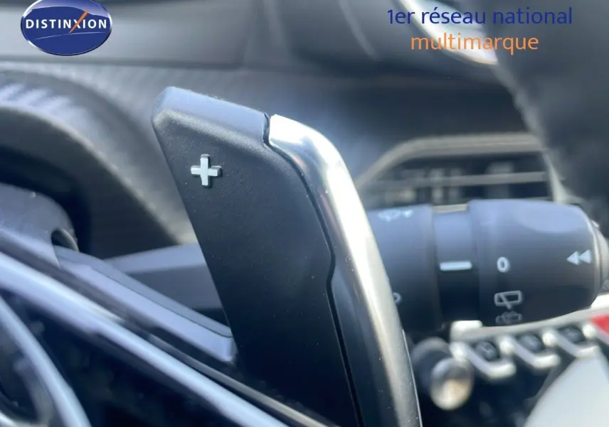 Gros plan sur la palette de changement de vitesse + du Peugeot 2008 gris Artense, intérieur moderne et commandes au volant.