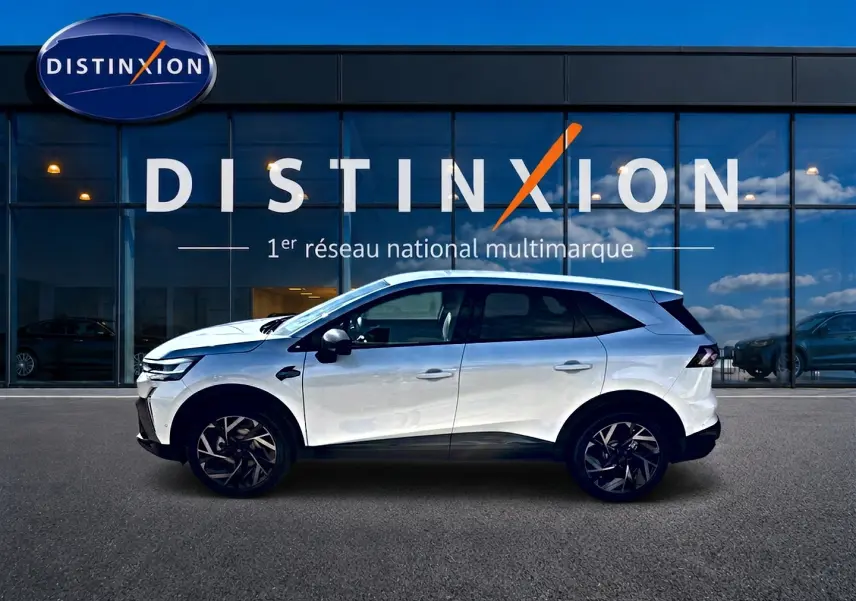 Profil droit du Renault Symbioz blanc nacré 2026 devant une vitrine Distinxion, soulignant ses jantes alu noires.
