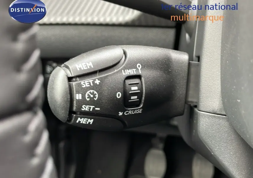 Gros plan sur la commande de régulateur de vitesse à gauche du volant dans une Peugeot 208 noire Perla Metal 2024.