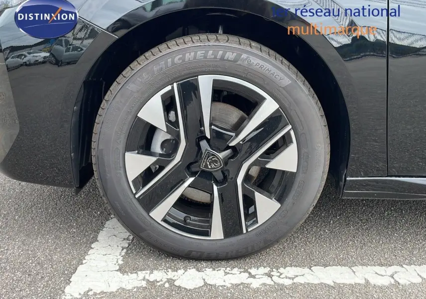 Gros plan sur la roue avant gauche d'une Peugeot 208 noire Perla Metal avec jante alliage bicolore moderne.