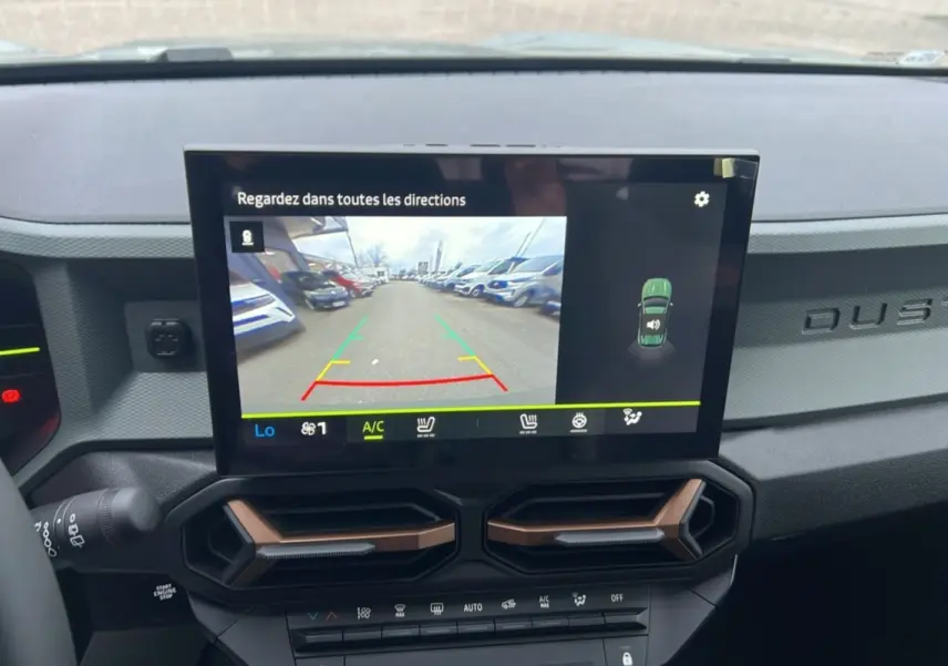 Vue intérieure du tableau de bord du Dacia Duster 2025 avec écran tactile affichant la caméra de recul et aérateurs hexagonaux.
