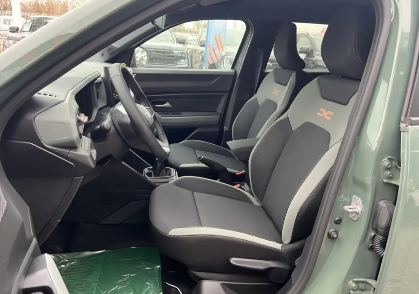 Intérieur côté conducteur du Dacia Duster 2025 kaki lichen, montrant les sièges sport avec logo orange et tableau de bord moderne.