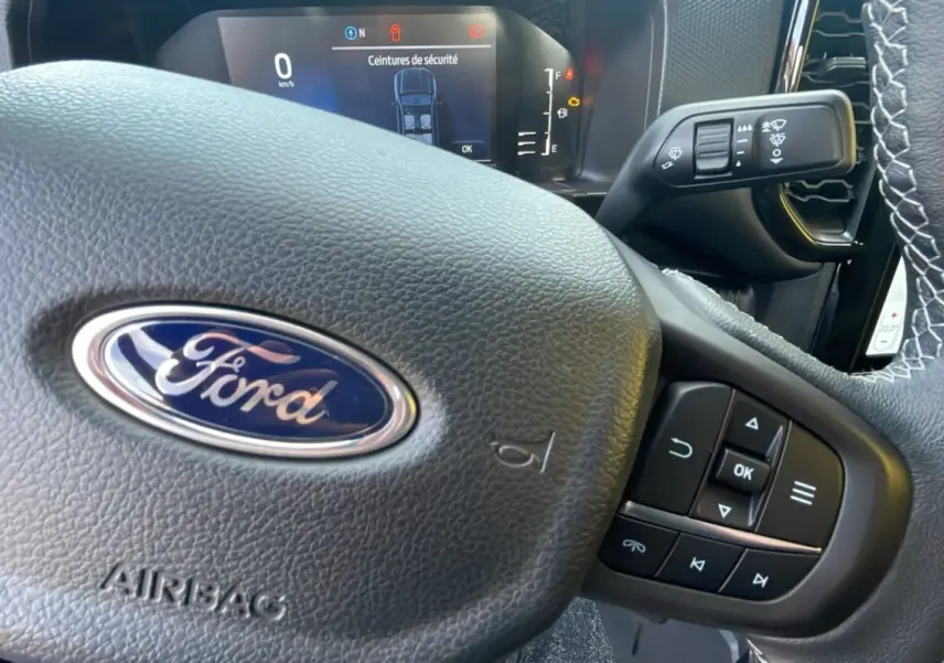 Gros plan sur le volant en cuir noir du Ford Ranger 2025 avec commandes multifonctions et tableau de bord numérique visible.