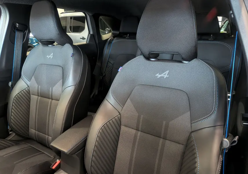 Vue intérieure rapprochée des sièges avant noirs avec surpiqûres bleues et logo Alpine sur les appuie-têtes.