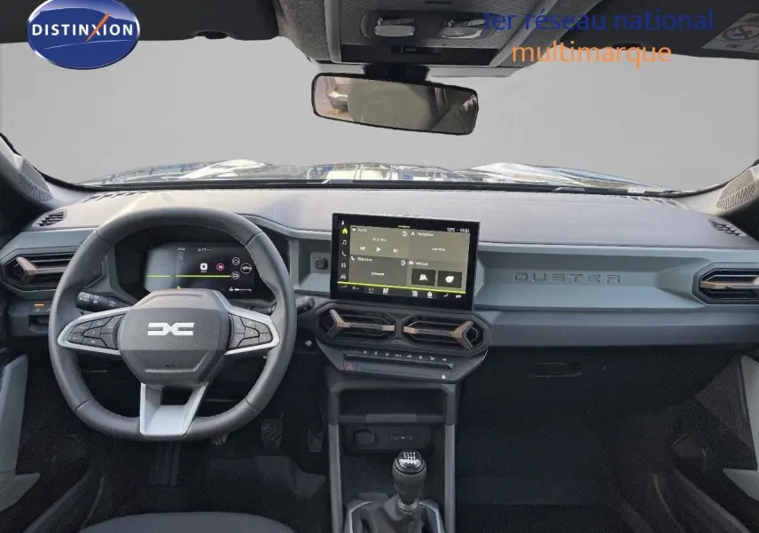 Tableau de bord noir du Dacia Duster 2024 avec volant multifonction, écran tactile et levier de vitesses manuel visible de face.