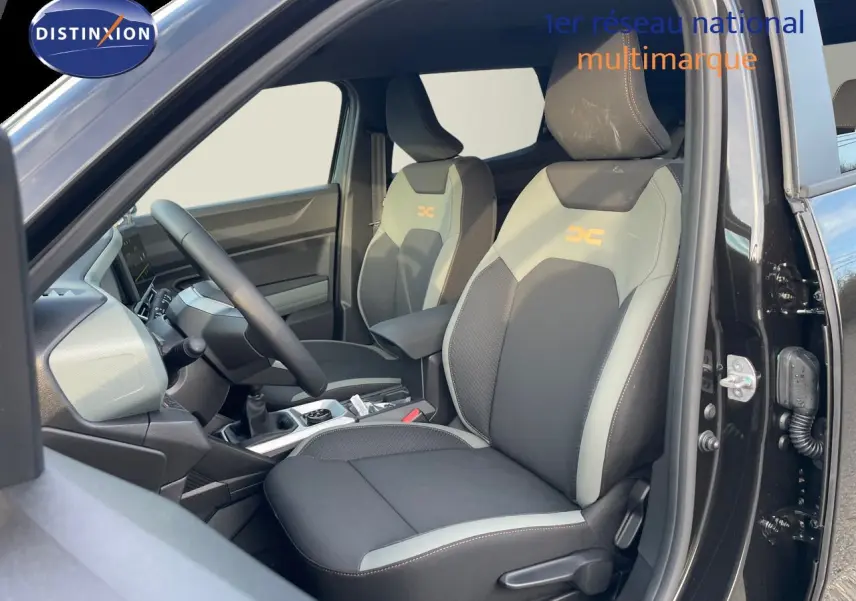 Vue intérieure côté conducteur du Dacia Duster 2024 noir métal, sièges bi-ton gris et noir avec logo orange DC.