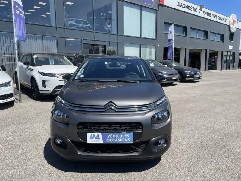 Citroën C3 gris foncé métal vue de face sur parking devant un garage avec panneau "Véhicules Occasions".
