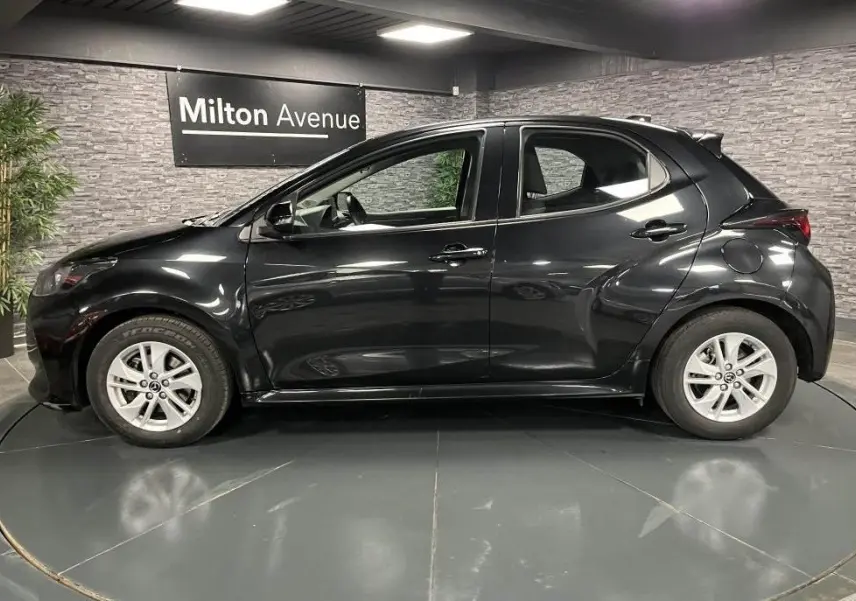 Vue de profil côté gauche d'une Mazda2 noire 2023 avec jantes alliage 15 pouces dans un showroom intérieur.