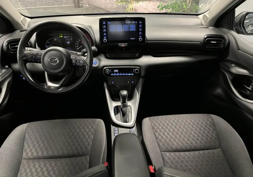 Intérieur noir de la Mazda2 2023, vue frontale sur le tableau de bord avec écran tactile et volant cuir multifonction.