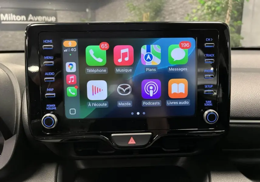 Écran tactile central de la Mazda2 2023 affichant Apple CarPlay avec commandes latérales et bouton de volume.