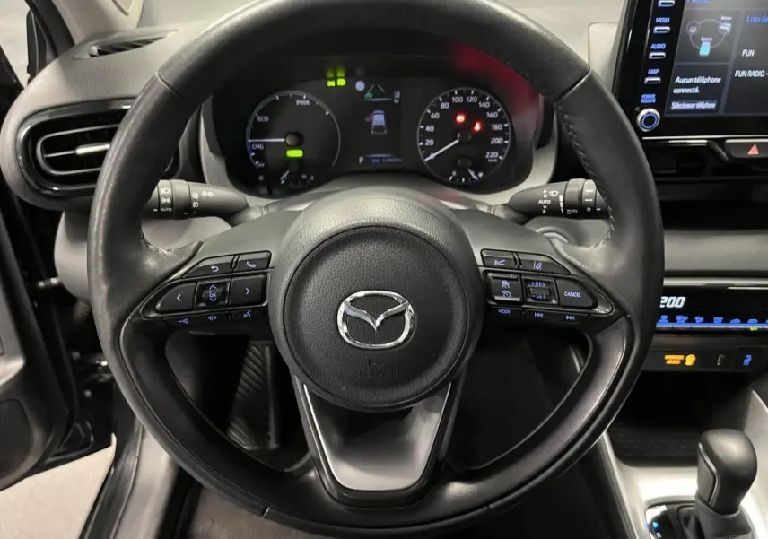 Vue frontale du volant en cuir noir de la Mazda2 2023 avec commandes intégrées et tableau de bord digital lumineux.