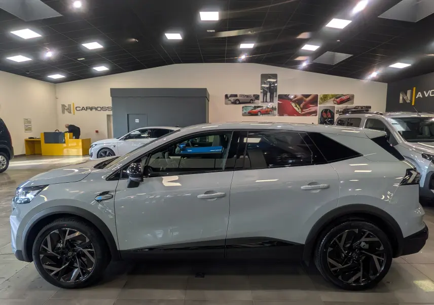 Vue de profil côté gauche d’un Renault SYMBIOZ gris Rafale avec jantes noires et toit noir dans un showroom.