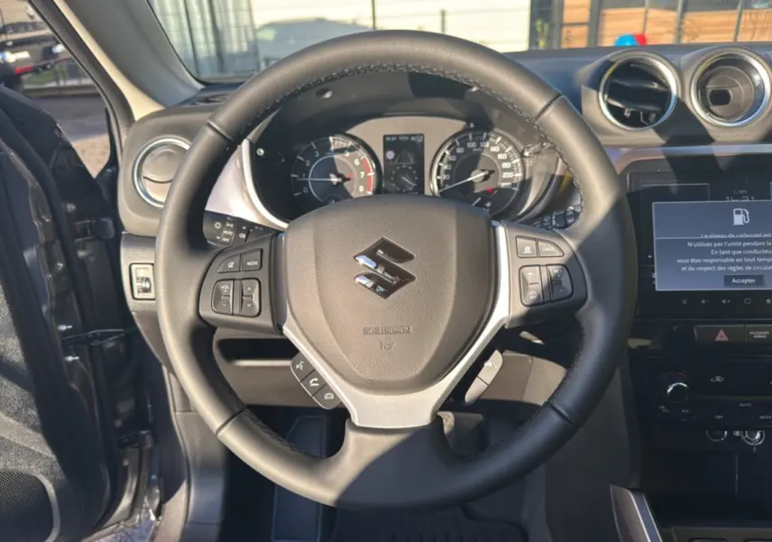 Vue intérieure centrée sur le volant cuir multifonctions du Suzuki Vitara Hybrid 110 Privilege AllGrip gris Titan.
