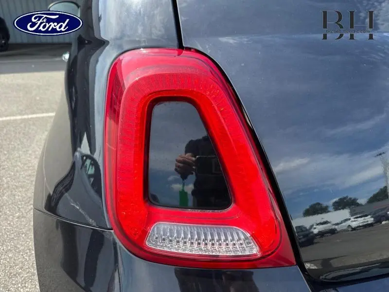 Gros plan sur le feu arrière droit rouge de la FIAT 500 Lounge 2018 en Crossover Black Métal, avec reflet du ciel et environnement.
