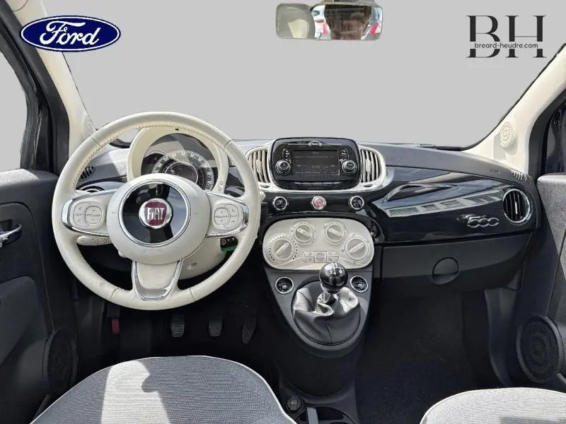 Vue intérieure avant du tableau de bord noir brillant et volant beige de la Fiat 500 Lounge 2018 avec boîte manuelle.