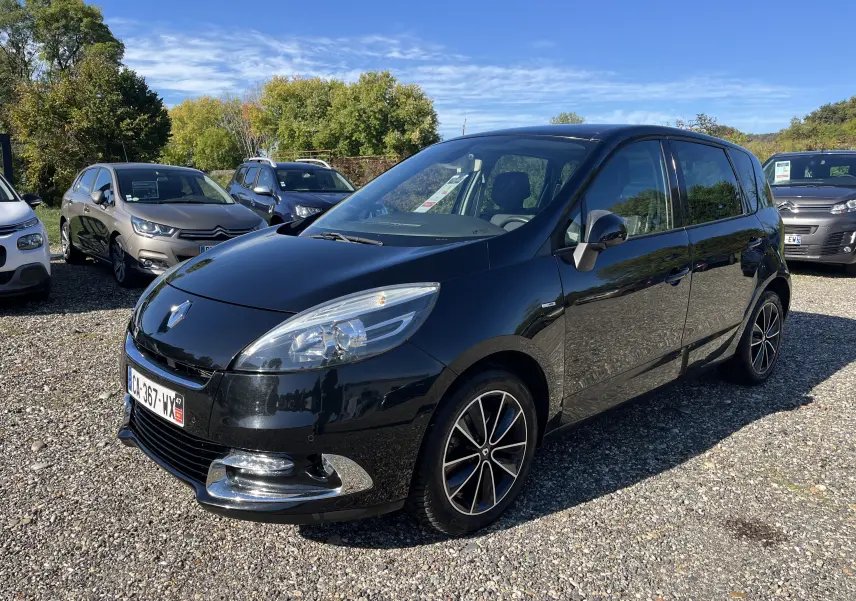 Renault Scenic III noir en 3/4 avant droit, avec jantes alliage et calandre chromée brillante sous un ciel dégagé.