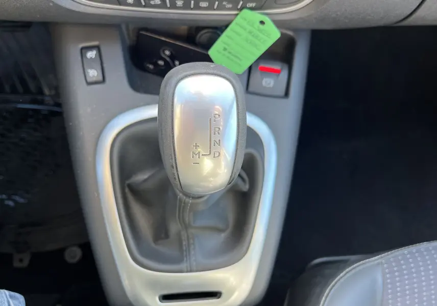 Gros plan sur le levier de vitesses automatique argenté du Renault Scenic III noir, avec console centrale et siège tissu visible.