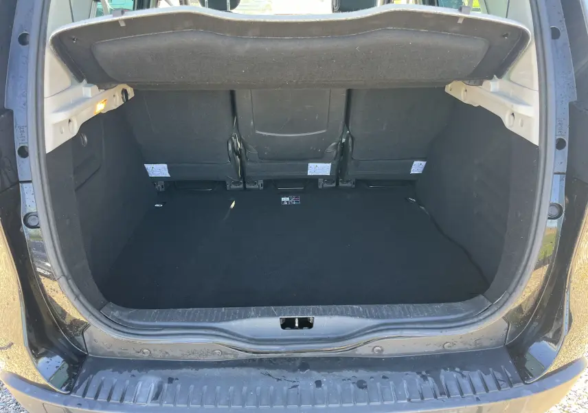 Coffre ouvert vu de l'arrière d'un Renault Scénic III noir, montrant l'espace de chargement et les dossiers des sièges arrière.