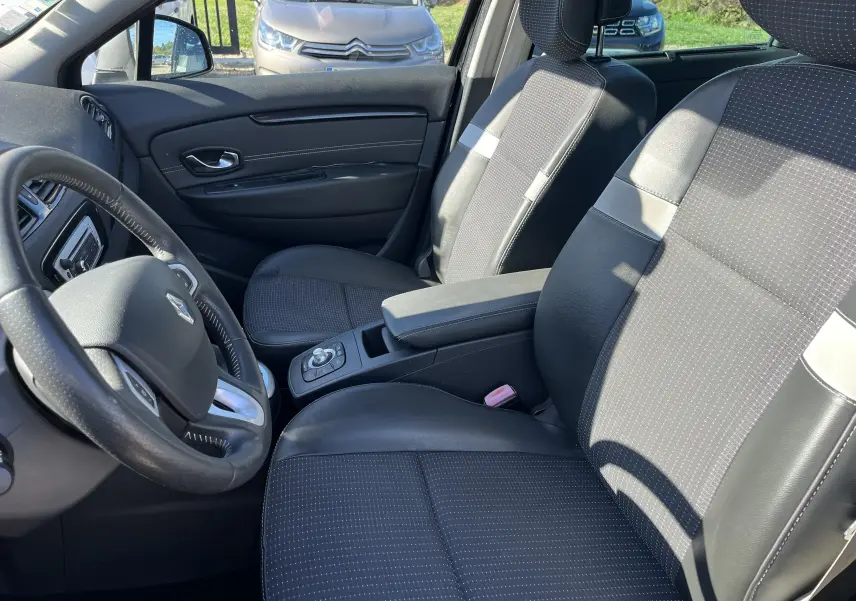 Intérieur de Renault Scénic III 2012 en vue latérale gauche, sièges tissu et cuir noir avec console centrale et volant visible.