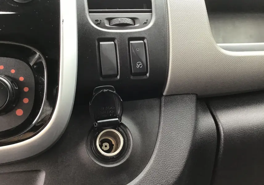 Prise allume-cigare ouverte sur le tableau de bord noir et gris du Renault Trafic Planche cabine blanc, version frigorifique.