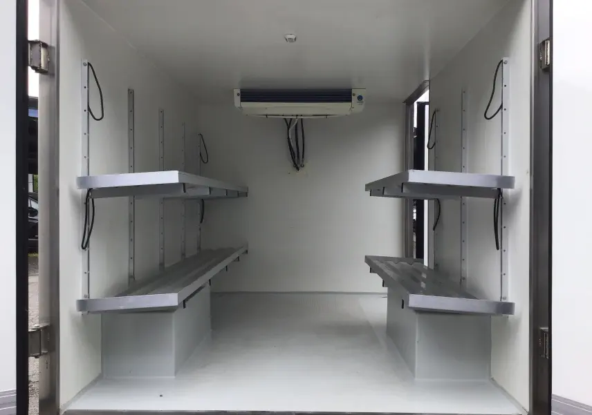 Intérieur de la caisse frigorifique blanche du Renault Trafic Planche cabine, vue arrière avec étagères métalliques et groupe froid au plafond.