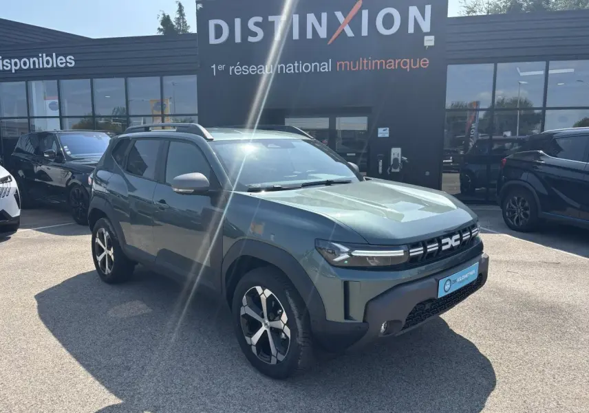 SUV Dacia Duster vert cèdre métal en 3/4 avant droit, avec jantes alliage et barres de toit visibles.