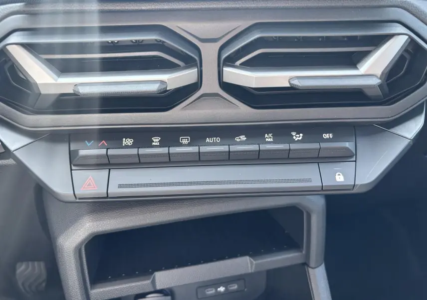 Gros plan sur la console centrale du Dacia Duster 2025, avec commandes climatisation et aérateurs hexagonaux noirs.